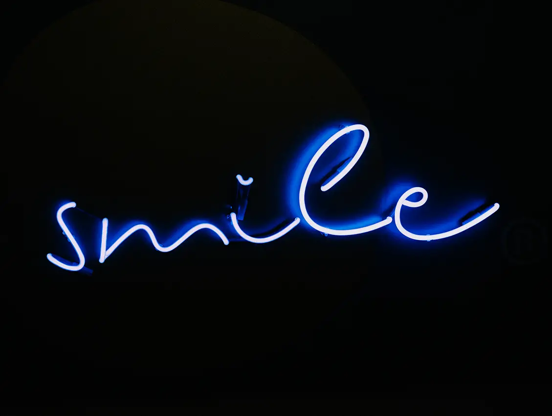Leuchtschrift mit dem Wort „smile“ in blauer Schreibschrift auf dunklem Hintergrund – visuelles Markenzeichen bei Kieferorthopäde Plattling und Teil des Gestaltungskonzepts der Praxis.