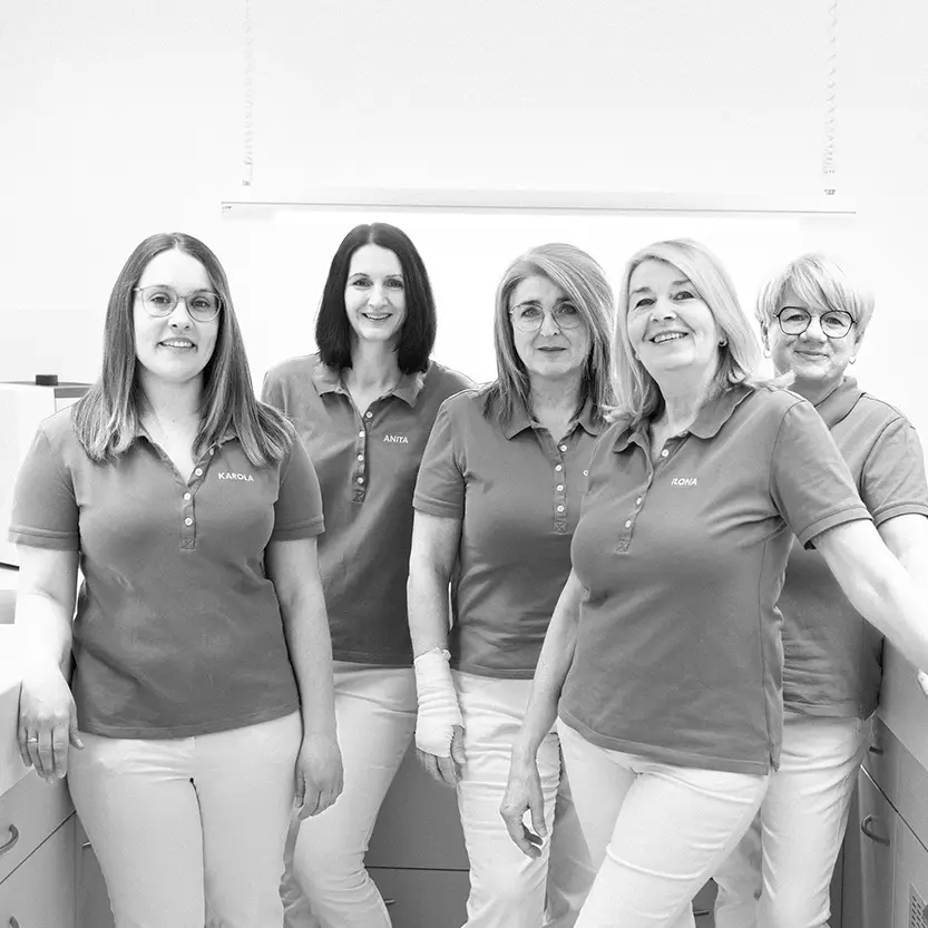 Fünf Frauen in medizinischer Arbeitskleidung stehen nebeneinander in einem hellen Behandlungsraum und lächeln in die Kamera