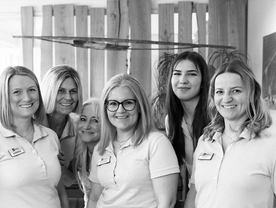 Praxisteam steht gemeinsam und lächelt in die Kamera