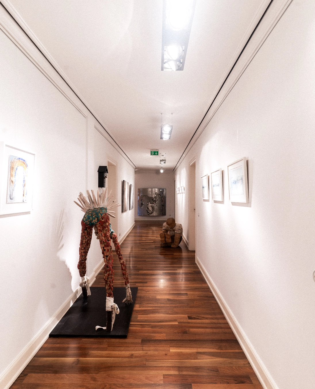 Langer Praxisflur mit Holzskulptur und Kunstwerken an den Wänden