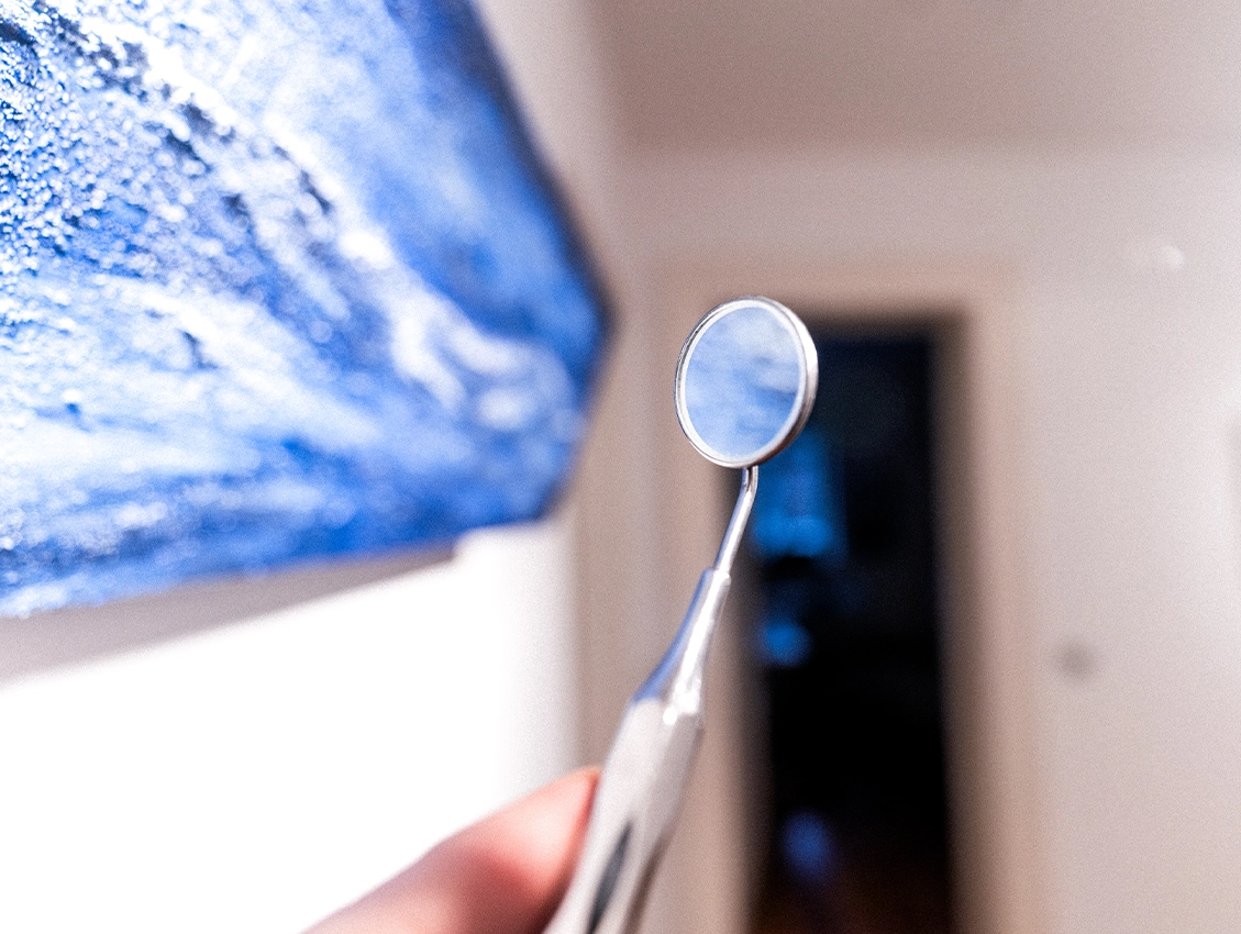 Zahnarztspiegel in der Hand vor unscharfem Hintergrund